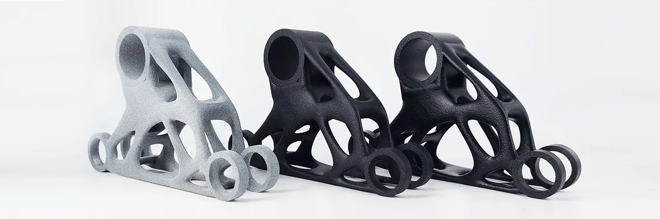 Drei topologieoptimierte 3D gedruckte Bauteile in Polyamid 12 ("PA 12") in Grau und Schwarz.