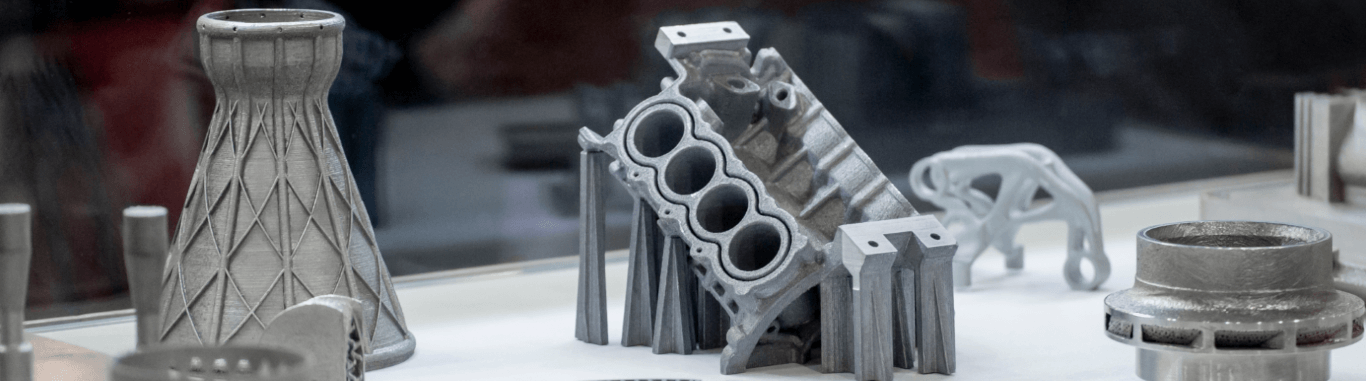 Several additively manufactured metal components made of 1.4404, with an angled engine block with support structures in the center.