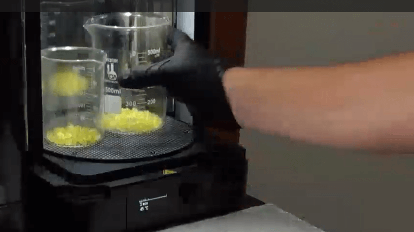 PµSL micro 3D printing: many small yellow parts in a beaker are placed in a UV exposure unit ('post-curing').